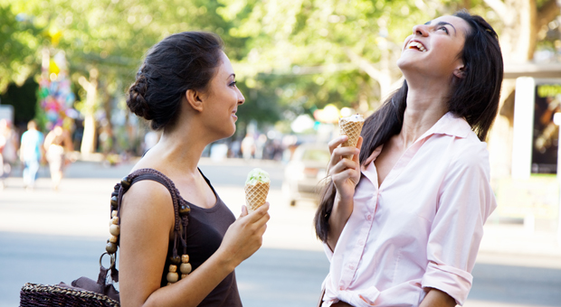 Foto på två kvinnor som äter glass och skrattar i stadsmiljö.