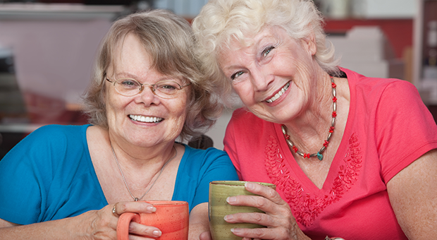 Två leende äldre kvinnor håller varsin porslinsmugg